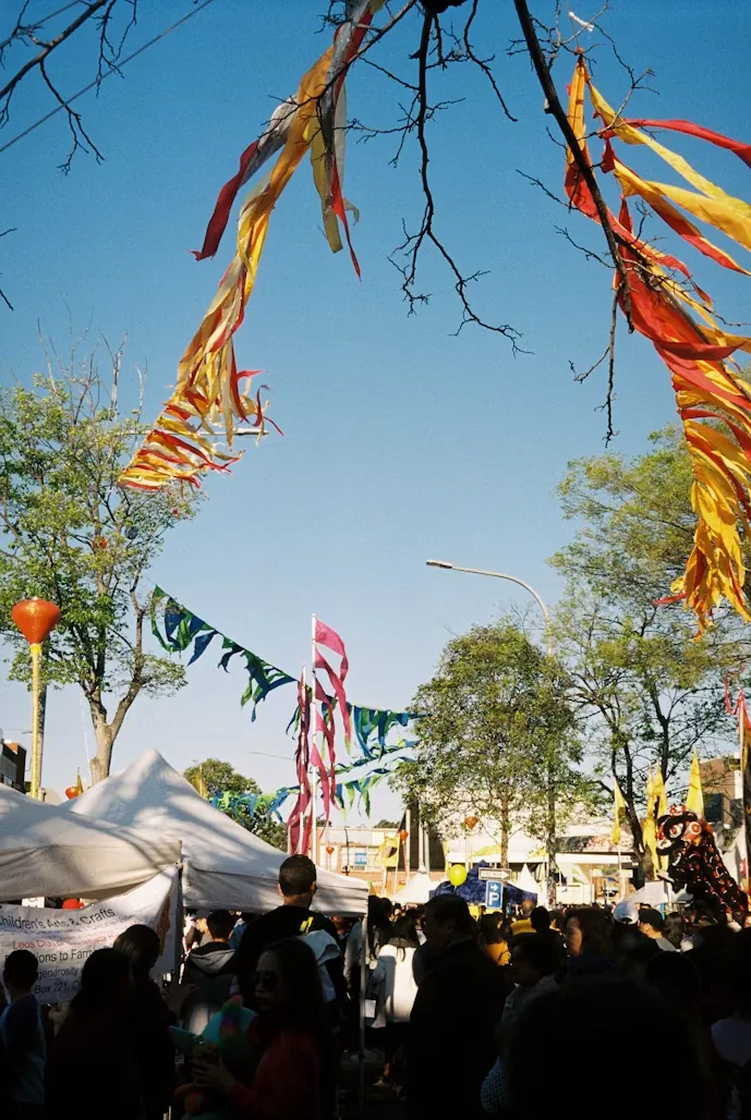 Colorful ribbon streamers and bunting strung above a crowded outdoor street festival on a clear day
