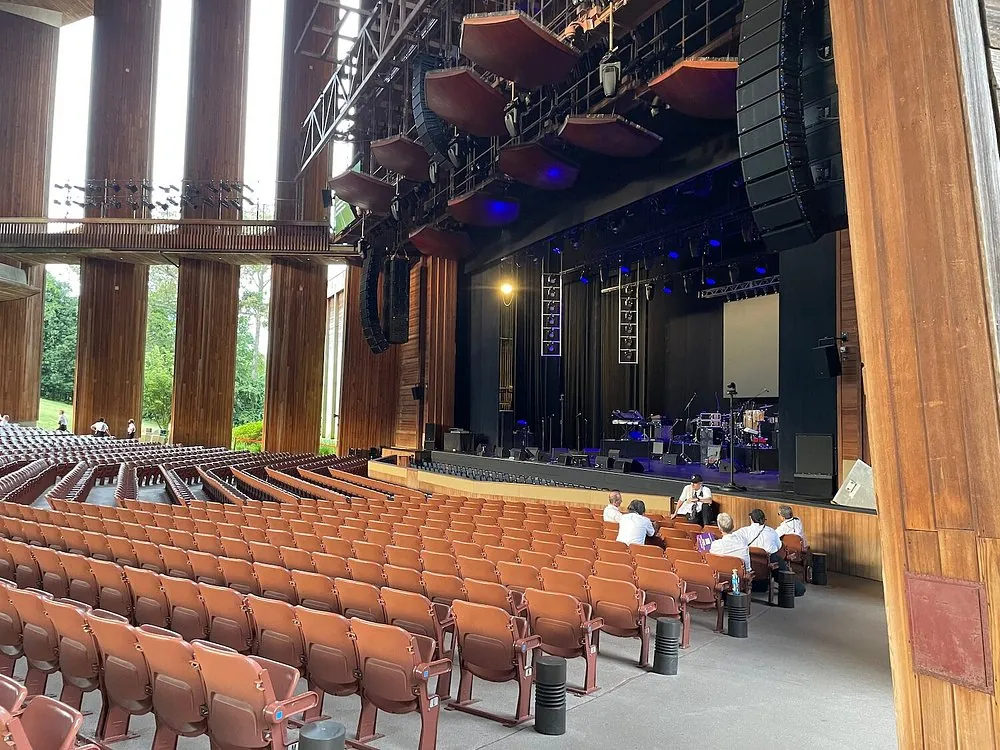 The open-sided wooden Filene Center at Wolf Trap, with tiered seats under the roof, the stage ahead and the woods visible through the side openings