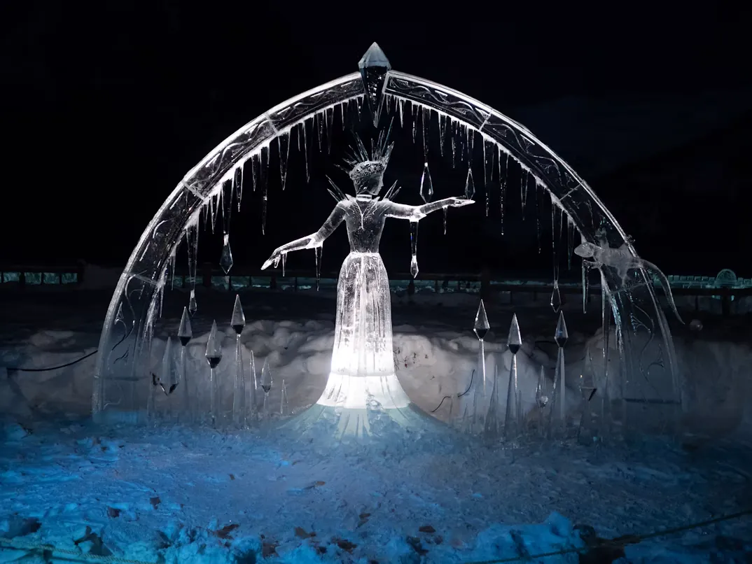 A glowing ice sculpture of a queen in a crown under an arch of icicles
