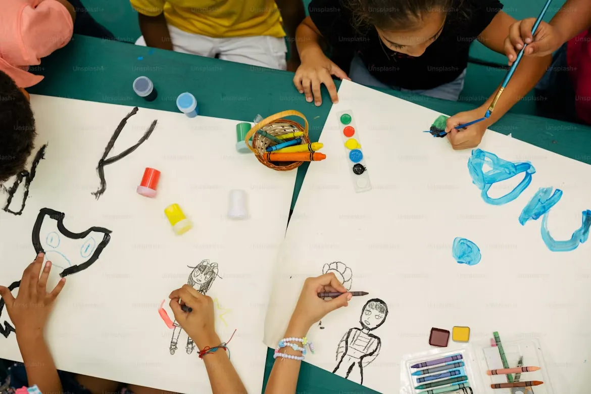 Kids painting and drawing together on big sheets of paper at a shared art table