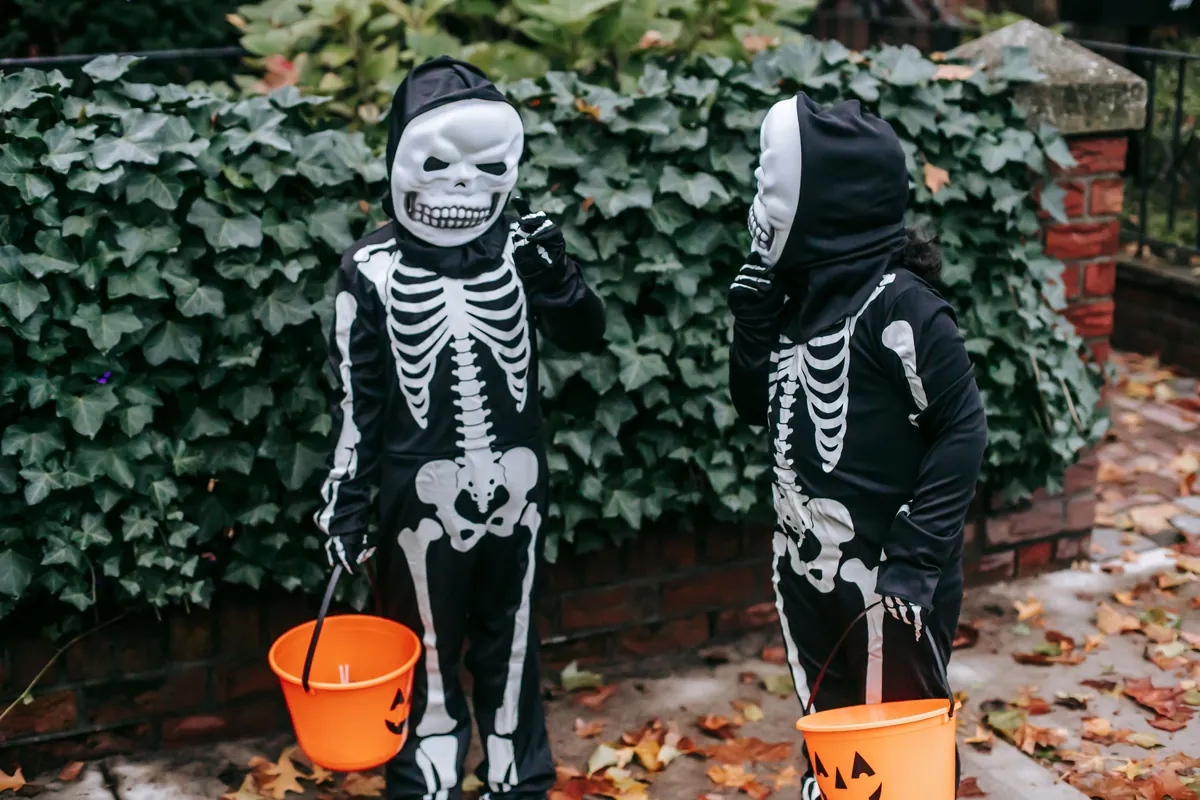 Two kids in skeleton costumes holding pumpkin candy buckets