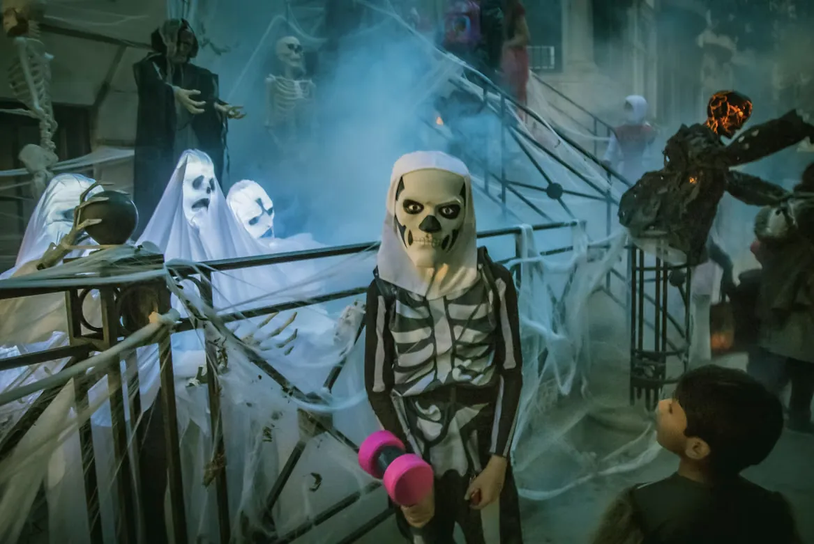 A child in a skeleton costume among ghost and skeleton Halloween decorations, with another child looking on