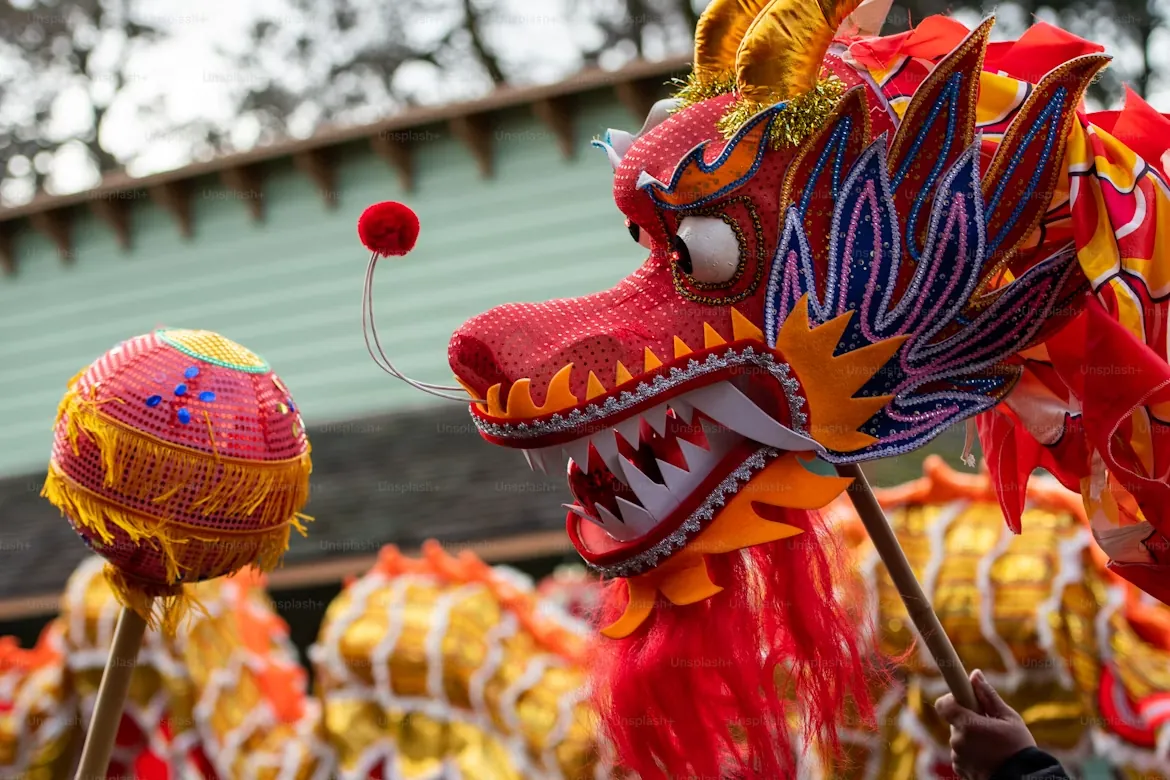 A bright red and gold Chinese dragon dance costume head with beaded detail, held up during a traditional street performance