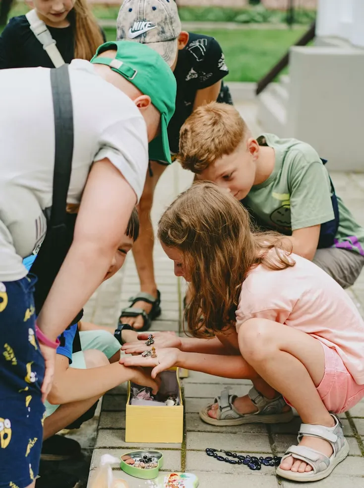 Kids crouched together on a sidewalk looking closely at something small in their hands